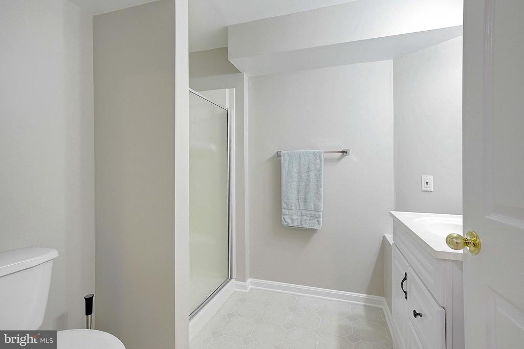 Bathroom with glass-enclosed shower, pale hexagonal tile, and white vanity.