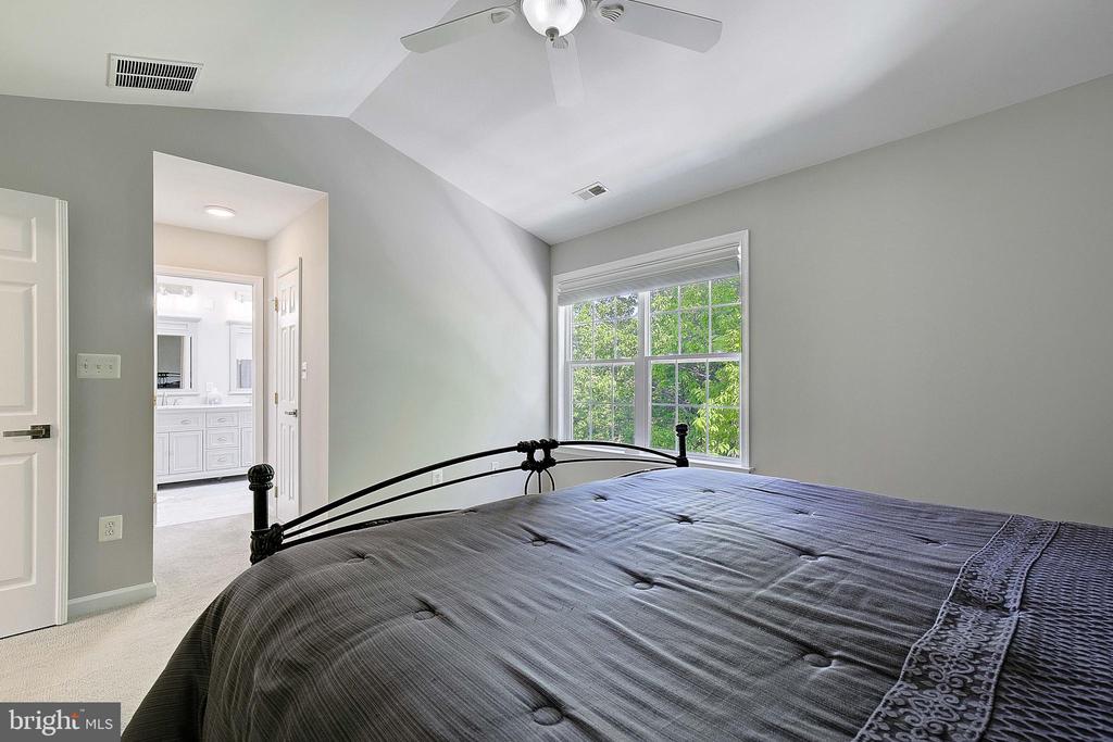 Bedroom with a black metal bed frame, ceiling fan, and window overlooking leafy trees.