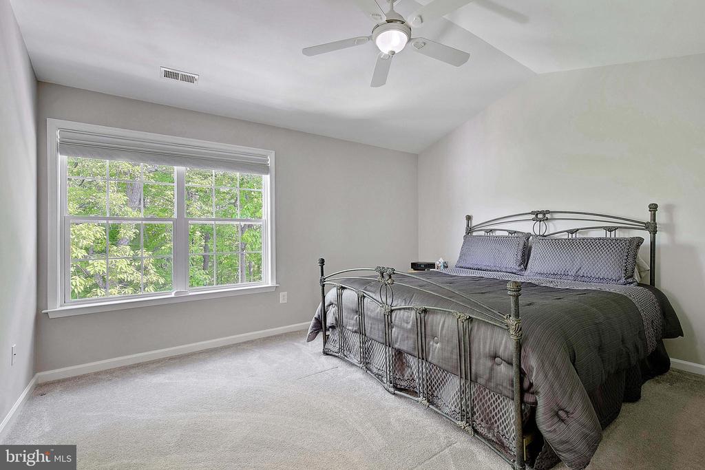 Bedroom with a metal bed, gray bedding, large window overlooking trees, and ceiling fan.