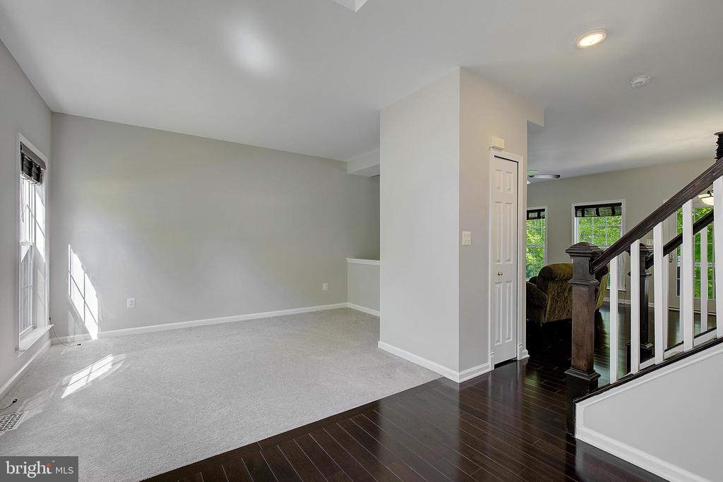 Empty carpeted living room beside a dark hardwood entry and staircase.