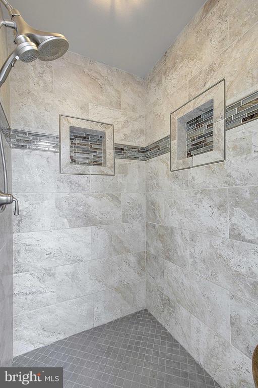 Walk-in shower with pale tile, two recessed niches, a mosaic floor, and chrome fixtures.
