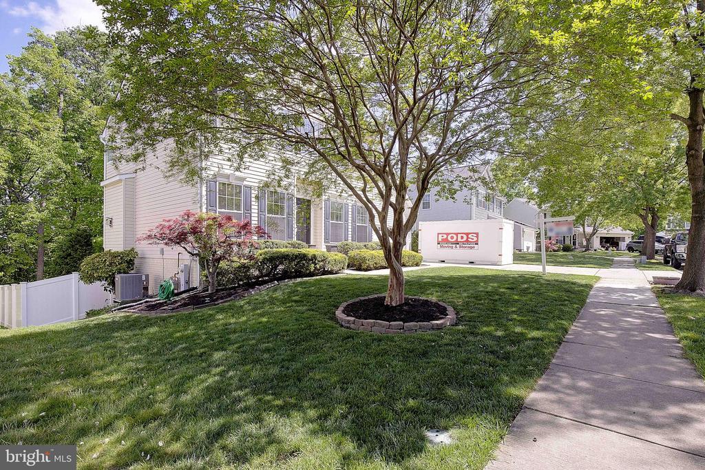 Townhouse exterior with a landscaped lawn, mature trees, sidewalk, and a PODS storage container.