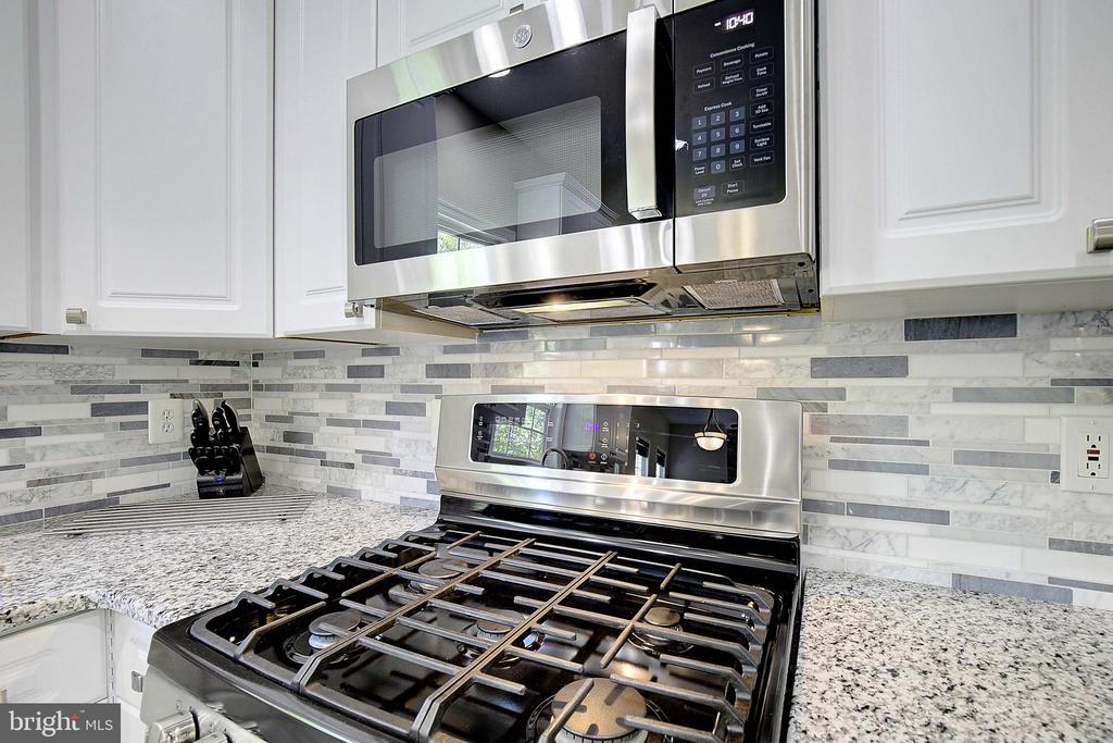 Kitchen with a stainless steel gas range, white cabinets, and gray-and-white mosaic backsplash.