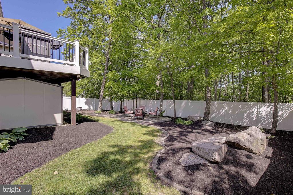 Backyard with a raised deck and patio seating beside a fenced, wooded yard.