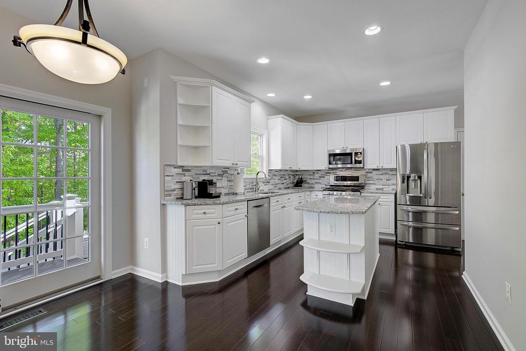 Kitchen with white cabinets, granite island, stainless steel appliances, and dark hardwood floors.