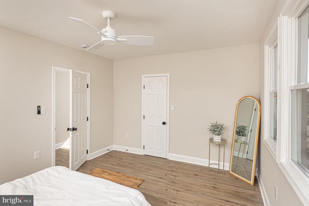 Bedroom with wood-look floors, tall windows, ceiling fan, and leaning floor mirror.