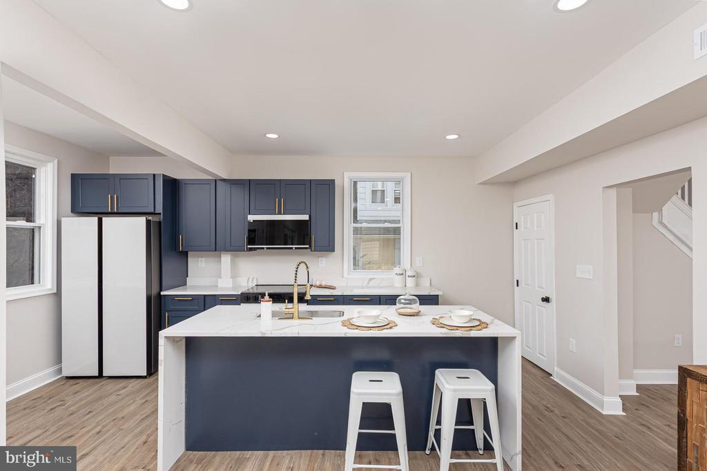 Kitchen with navy cabinets, a large white island, gold-tone faucet, and two white bar stools.