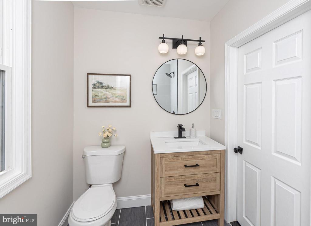 Bathroom with a light wood vanity, round mirror, and white toilet.