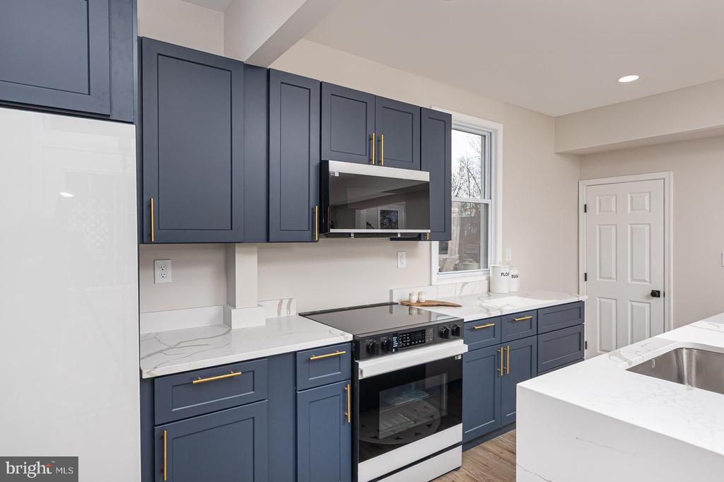 Kitchen with navy cabinets, brass pulls, marble-look counters, and stainless steel appliances.