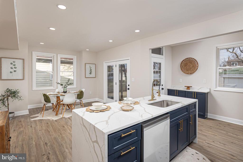 Open-plan kitchen with a navy island and white veined countertops beside a window-side dining table.