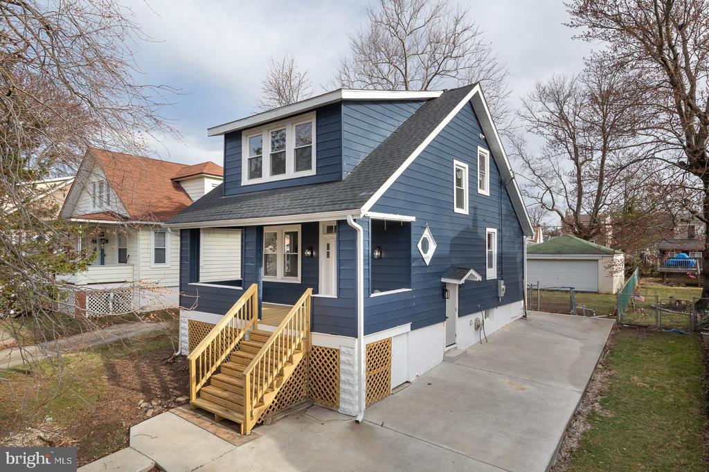 Blue-sided house with an upper dormer, raised wooden porch, and wide concrete driveway.