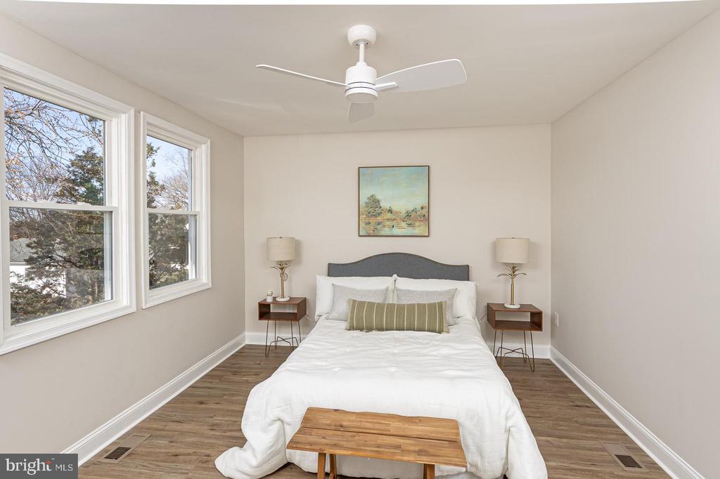 Staged bedroom with a white bed, two tall windows, and wood-look flooring.