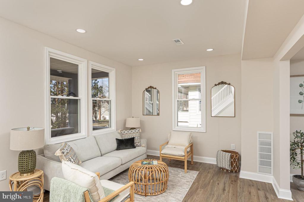 Staged living room with a gray sofa, wicker coffee table, large windows, and wood-look flooring.