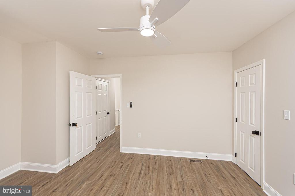 Empty room with wood-look flooring, a ceiling fan, and multiple white doors.
