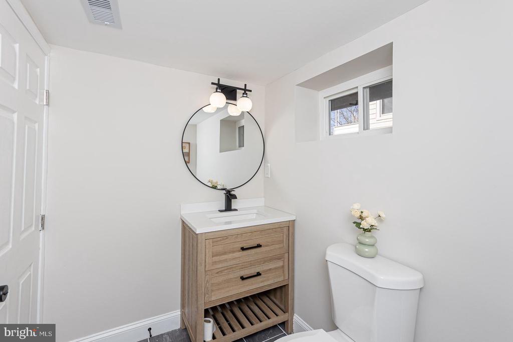 Bright bathroom with a wood vanity, round mirror, globe lights, and high window.
