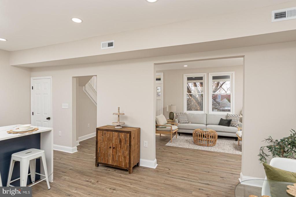 Open-plan living room with a gray sofa, two windows, wood-look floors, and a kitchen island.
