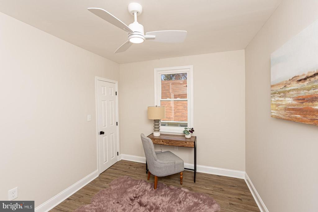 Staged home office with a wood desk beneath a window and a gray upholstered chair.