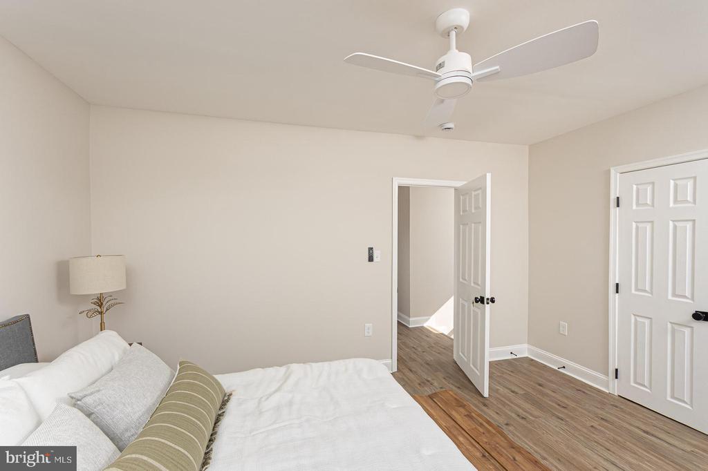 Bedroom with a white bed, ceiling fan, and open doorway to a hallway.