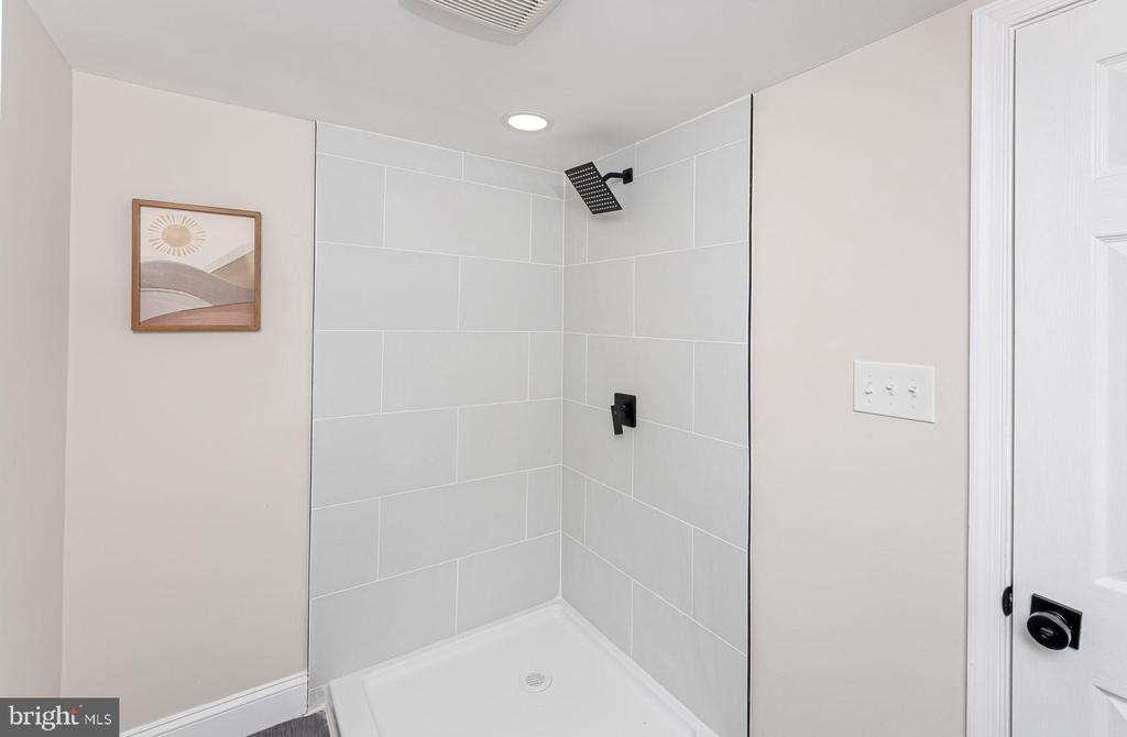 Tiled shower with black fixtures and a white base in a bright bathroom.