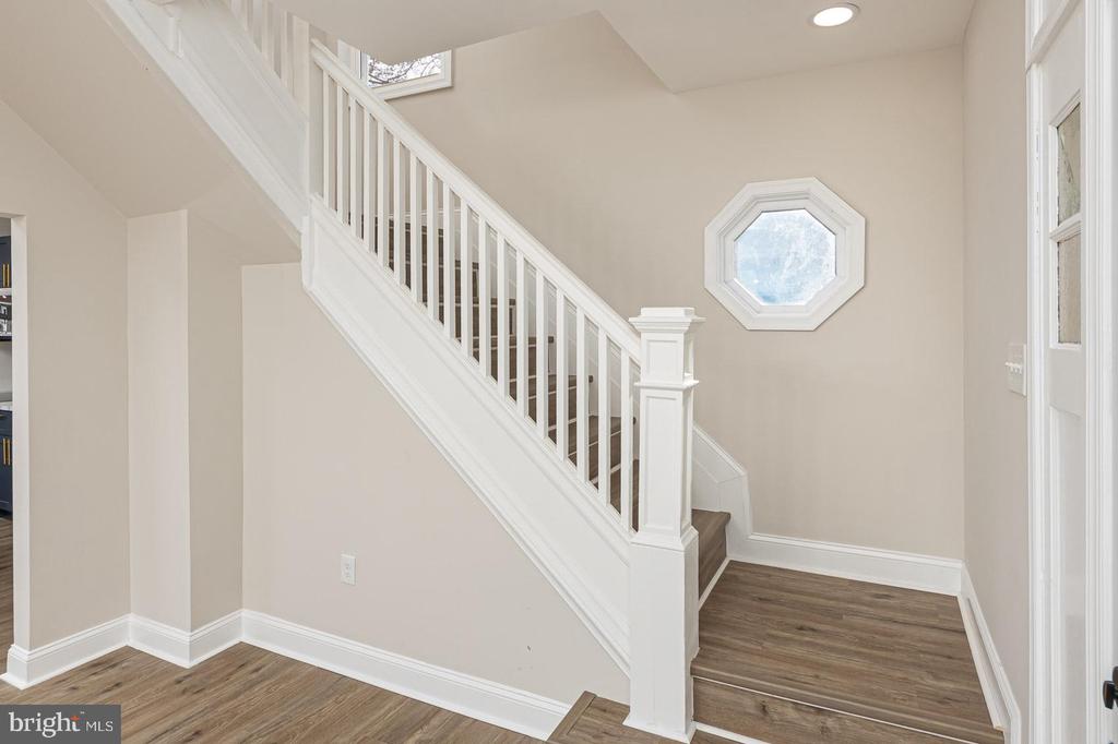 Entry hall with a white staircase, dark wood flooring, and an octagonal window.