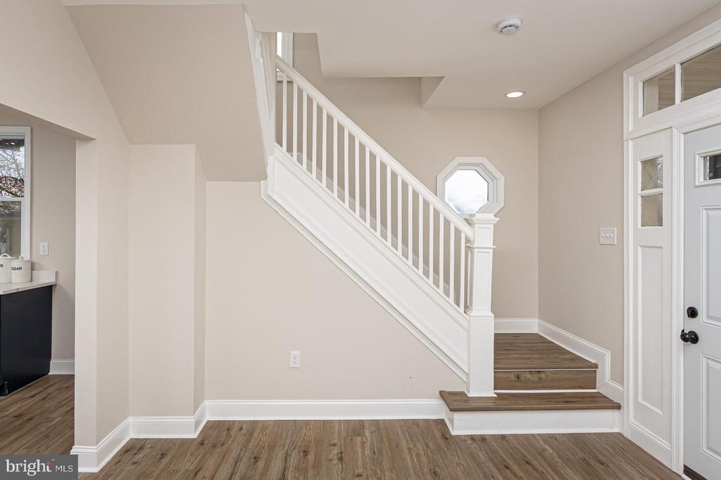 Entry foyer with a white staircase, wood-look flooring, and a front door with sidelights.
