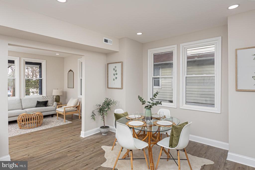 Dining room with a glass-top table and white chairs beside a living room with a gray sofa.