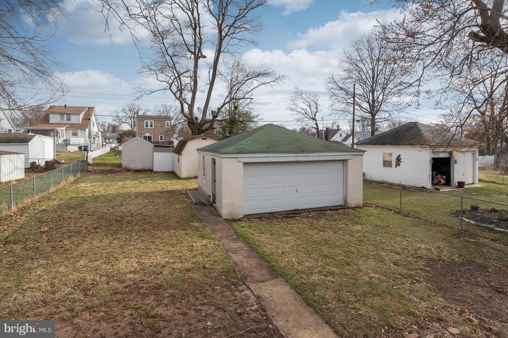 Detached white two-car garage with a green roof in a fenced yard.