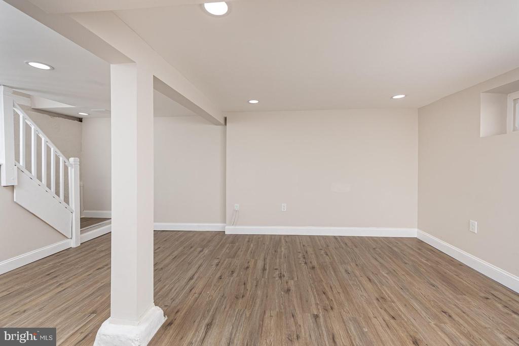 Vacant basement room with wood-look flooring, a white support column, and stairs.