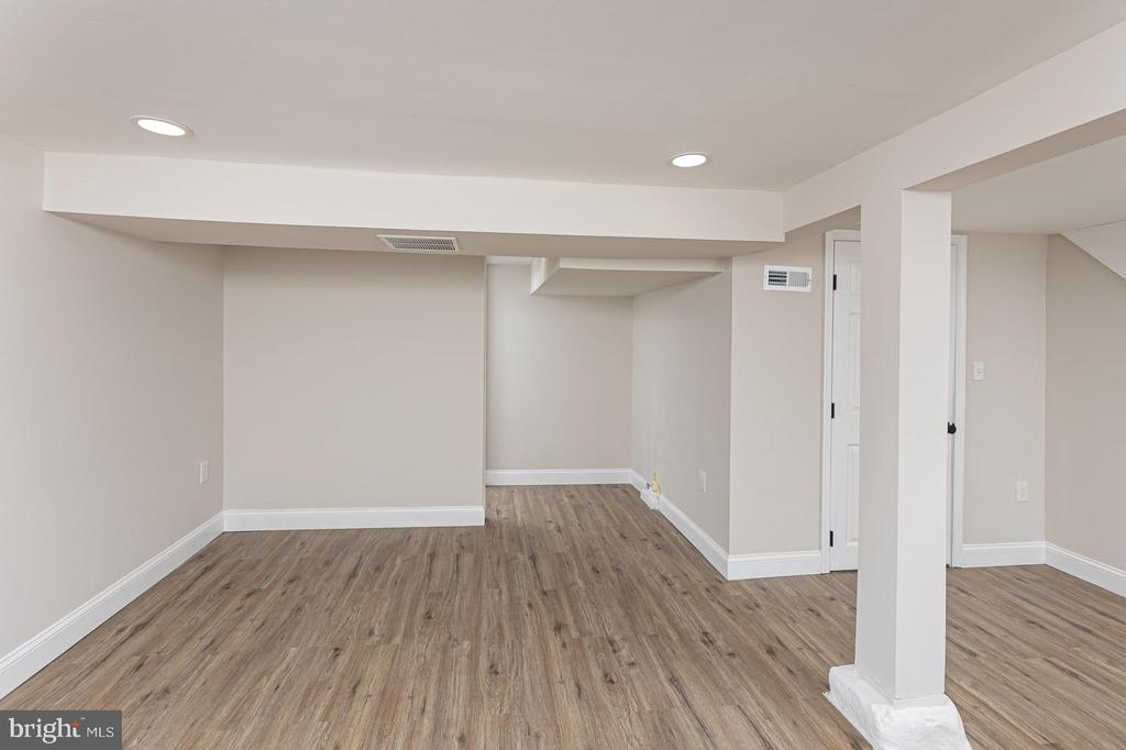 Vacant interior room with wood-look flooring, recessed lights, and a support column.