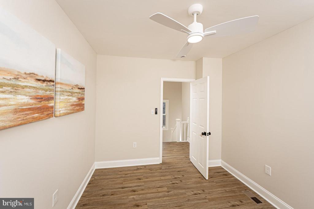 Empty room with wood-look flooring, a white ceiling fan, and an open door to the hallway.