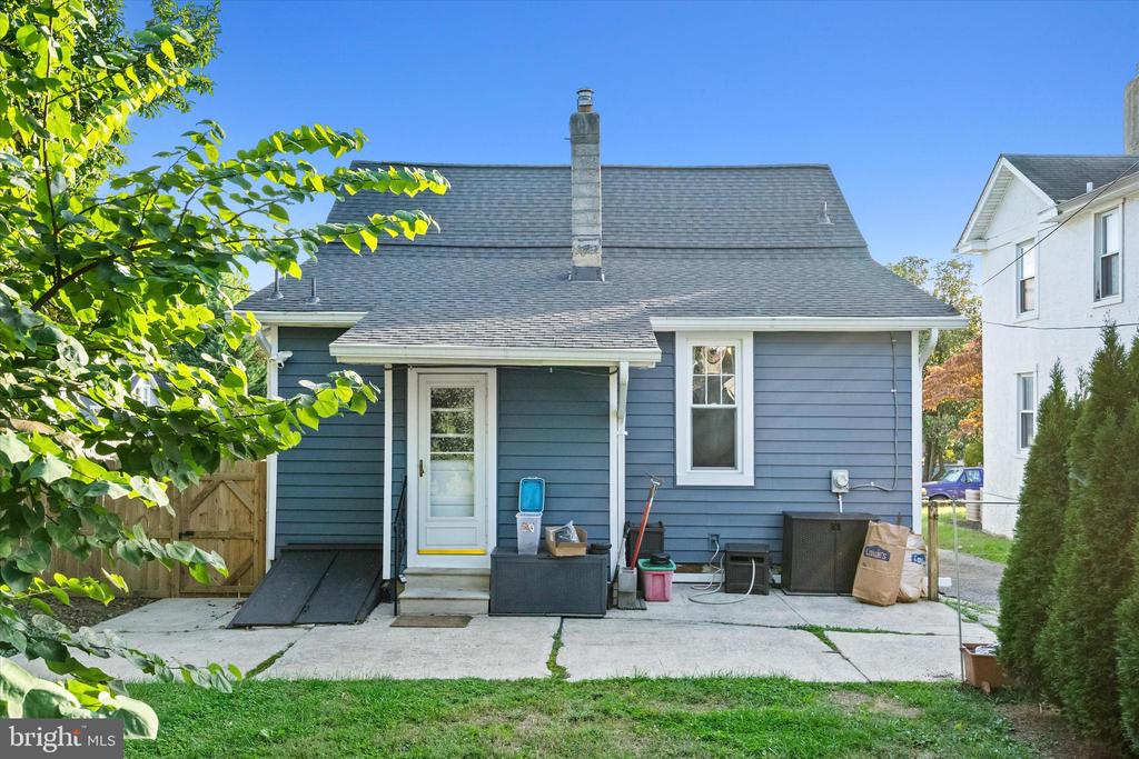 Blue-sided house with a covered rear entry, concrete patio, and chimney.