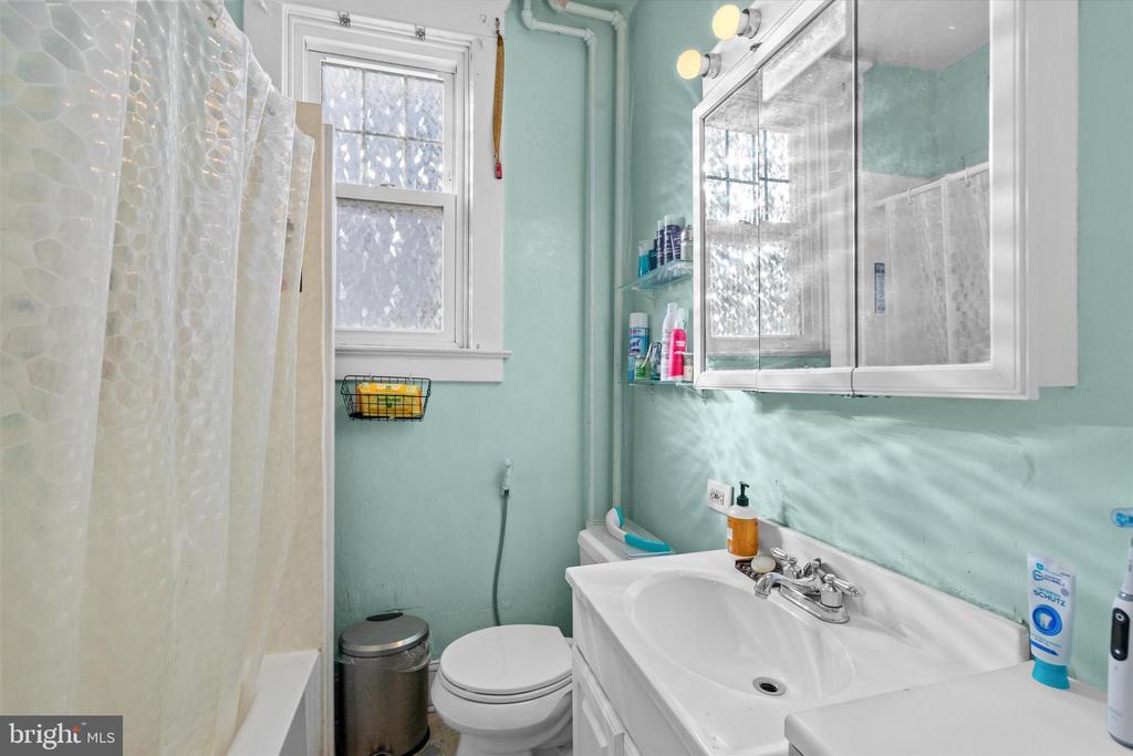 Bathroom with pale aqua walls, white vanity, mirrored cabinet, and patterned shower curtain.