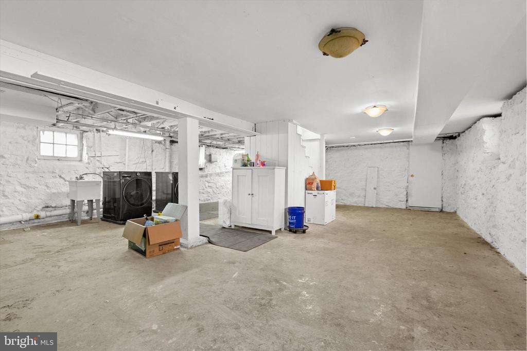 Basement laundry area with washer, dryer, utility sink, and exposed stone walls.