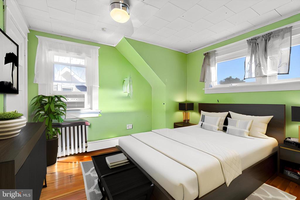 Bedroom with bright green walls, a large white bed, hardwood floors, and two curtained windows.