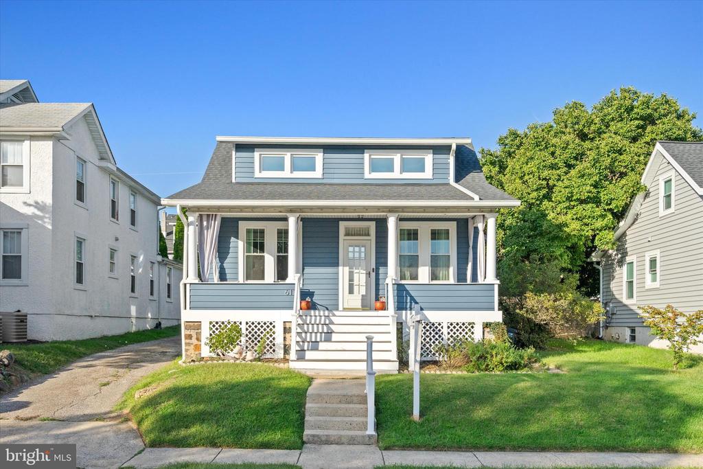 Blue-sided house with a covered front porch, upper dormer windows, and a green lawn.