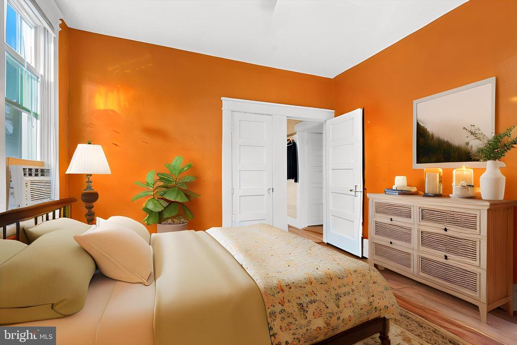 Bedroom with bright orange walls, a large pale bed, white closet doors, and a wooden dresser.
