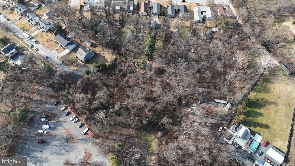 Aerial view of a wooded property bordered by neighborhood homes, parking areas, and open lawn.