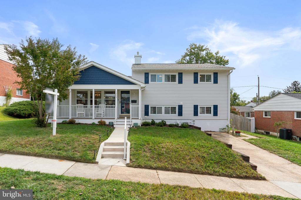 Two-story split-level house with a covered porch, blue shutters, front steps, and sloped lawn.