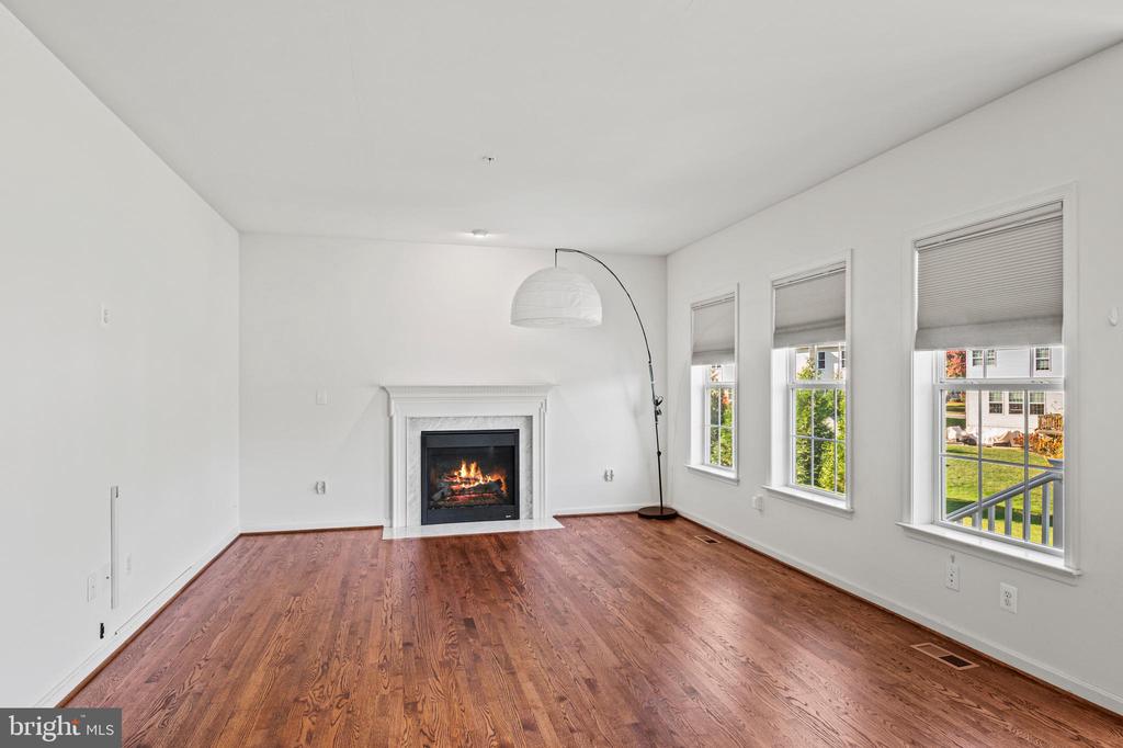 Empty living room with hardwood floors, a lit fireplace, and three windows with blinds.