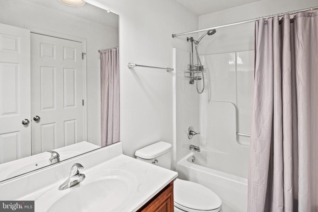 Bathroom with a white vanity and sink, toilet, and tub-shower behind pale pink curtains.