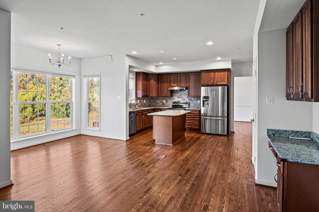 Open kitchen and dining area with hardwood floors, dark wood cabinets, and a granite island.