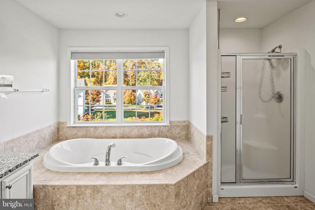 Bathroom with an oval soaking tub beneath a window and a glass-enclosed shower.