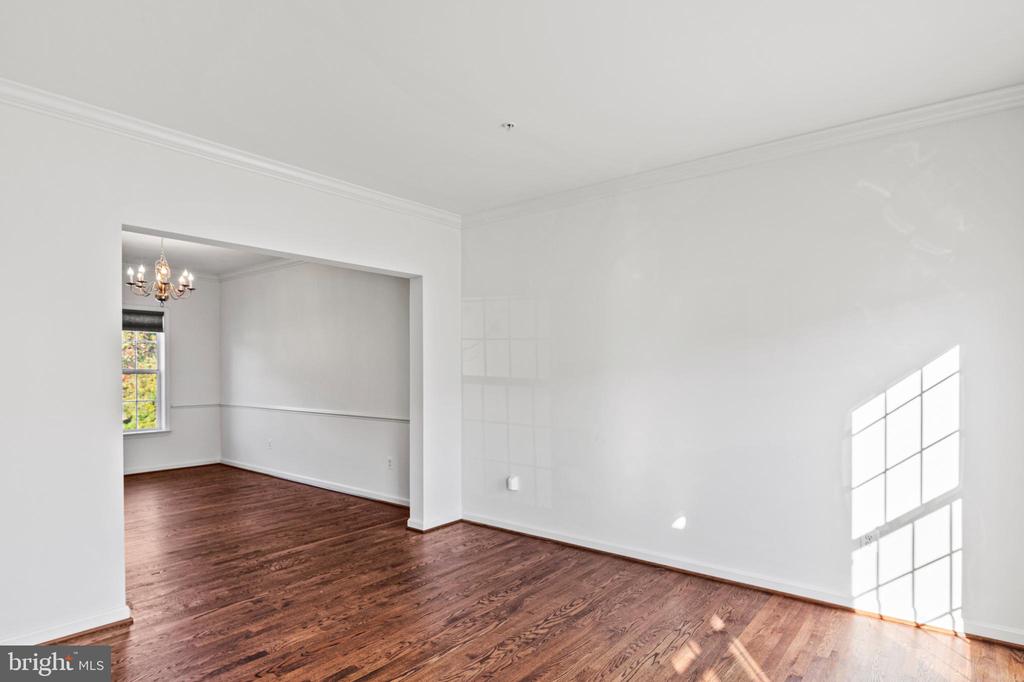 Vacant living room with hardwood floors and an opening to a chandelier-lit dining area.