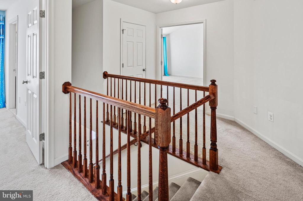 Carpeted upstairs landing with a dark wood railing around the stairwell.