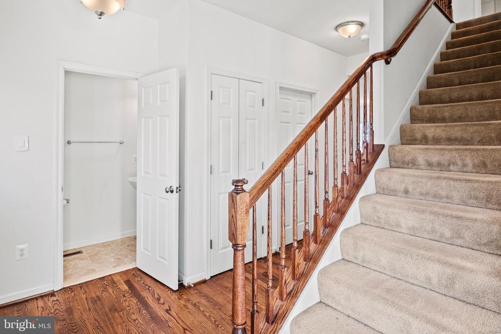 Stair hall with a carpeted staircase, polished wood banister, hardwood floor, and open bathroom doorway.