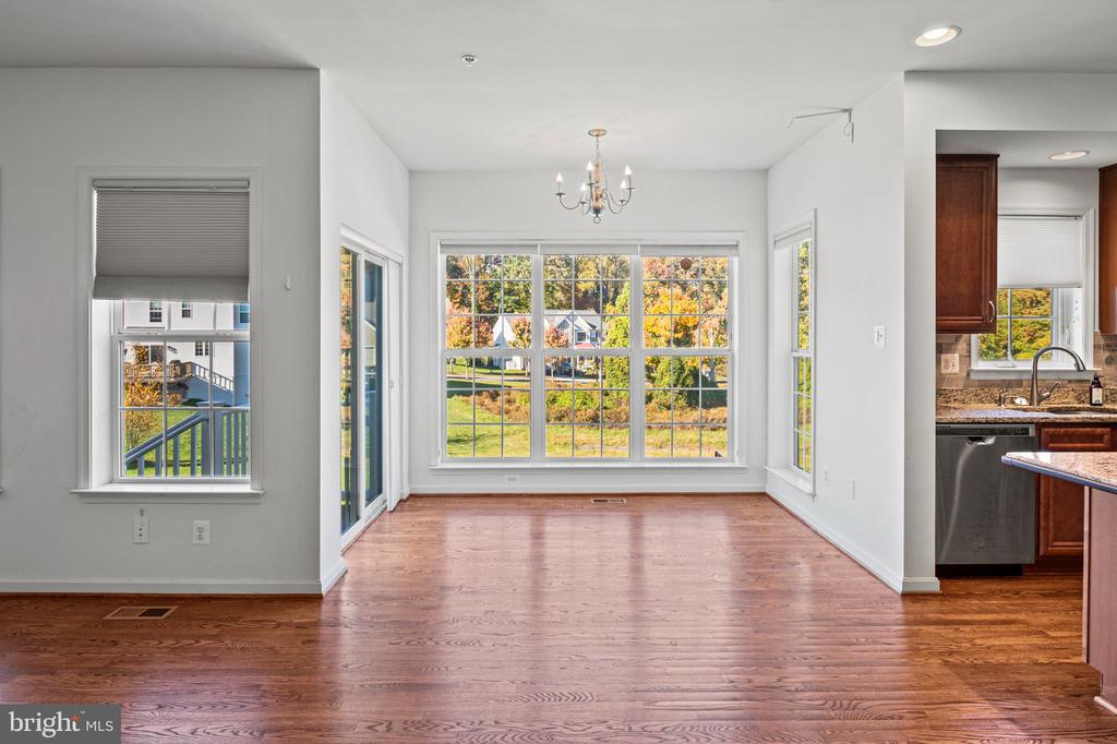 Empty dining area with hardwood floors, a chandelier, and large windows overlooking autumn foliage.
