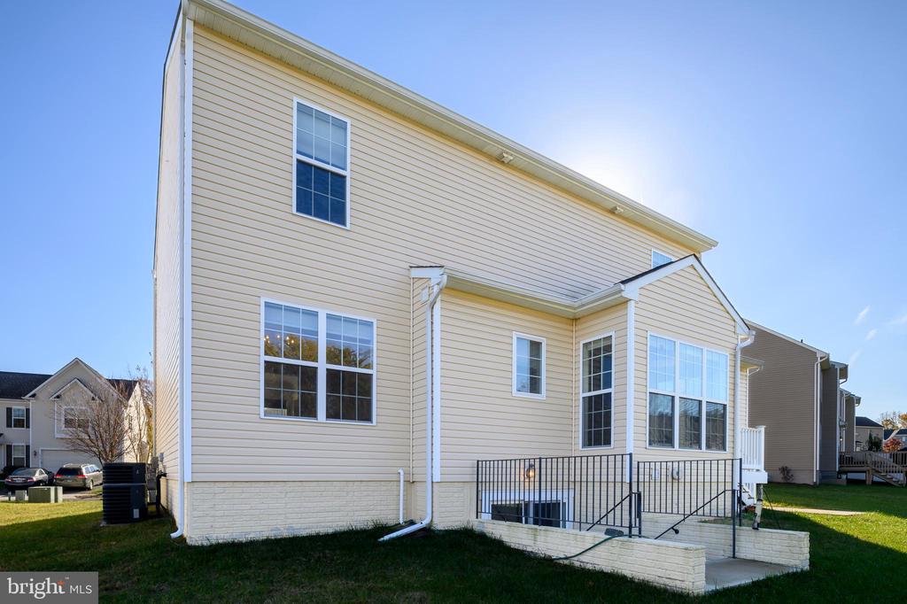 Rear exterior of a two-story beige house with large windows and a railing around the basement-level patio.