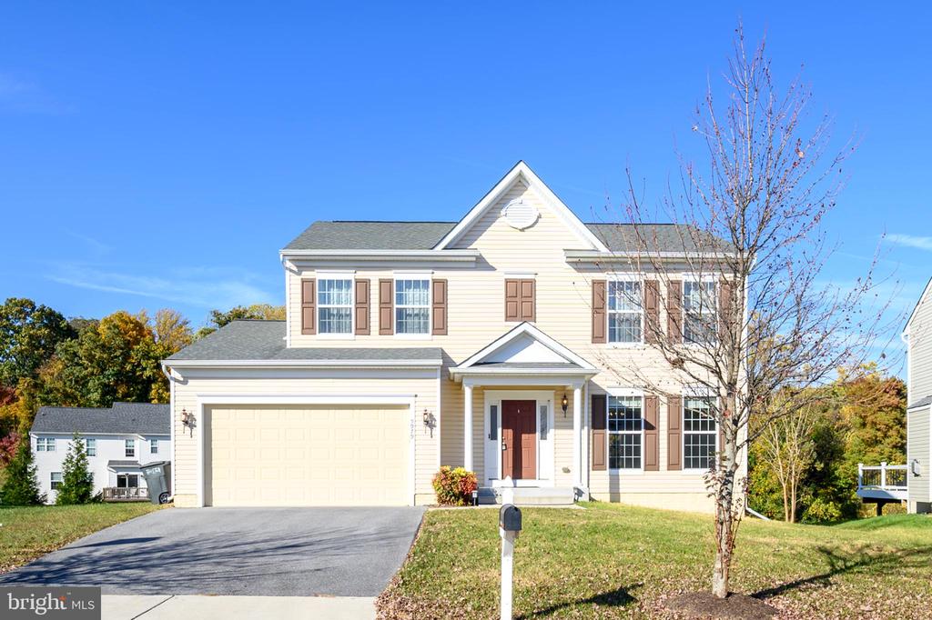 Two-story beige house with brown shutters, a double garage, and a covered front entrance.
