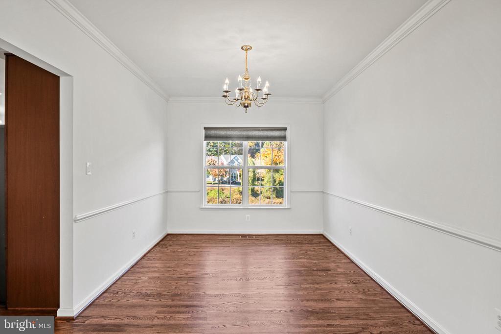 Empty dining room with hardwood floors, a brass chandelier, and a window overlooking autumn trees.