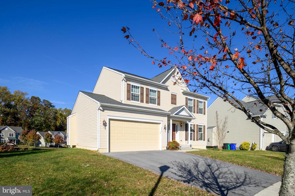 Two-story beige house with a double garage and covered entry, framed by an autumn tree.